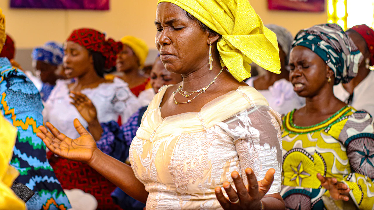 A woman in a yellow headwrap worshipping with her congregation